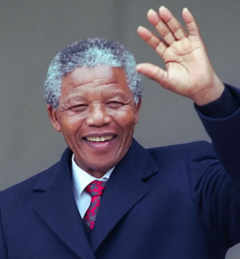 Nelson Mandela smiling and waving with raised hand wearing dark suit and red tie against neutral background